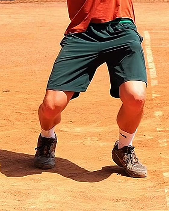 Pavel Viks with knees bent and hips lowered, loading his legs for the serve